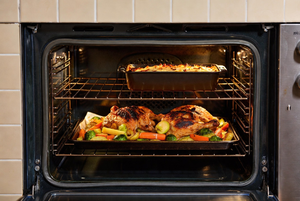 Open oven with a sheet-pan roast chicken, vegetables and a gratin cooking on two racks at once